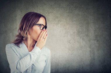 Gri duvar arka plan üzerinde gizli bir poz söylüyorum süre ağız kapsayan genç iş kadını. 