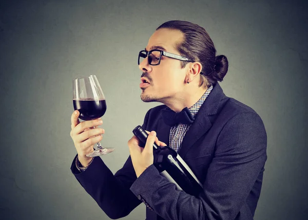 灰色の背景にアルコールに愛を探して赤ワインのグラスとボトルを保持している正式な皮肉な男 — ストック写真