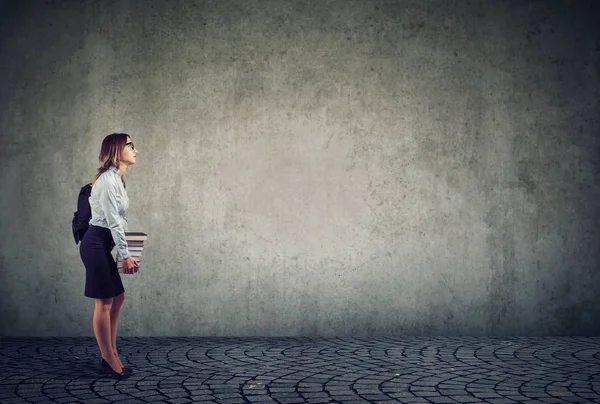 Sırt çantası ve gri arka plan üzerinde kitap yığını holding Gözlük Genç öğrenci yan görünüm