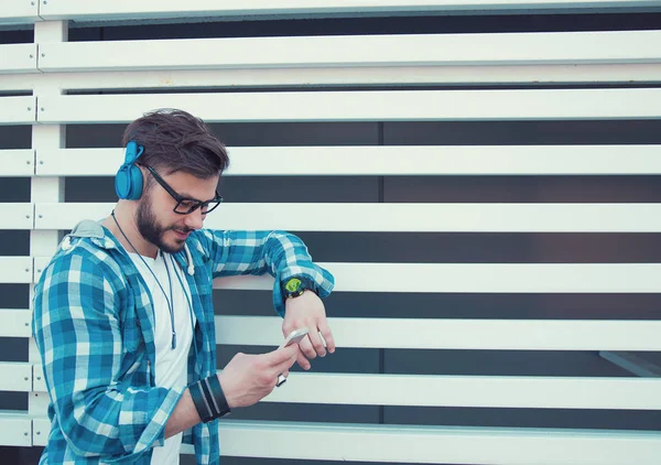 外に立っていると 音楽を聴きながらスマート フォンを使用してヘッドフォンでスタイリッシュな若者 — ストック写真