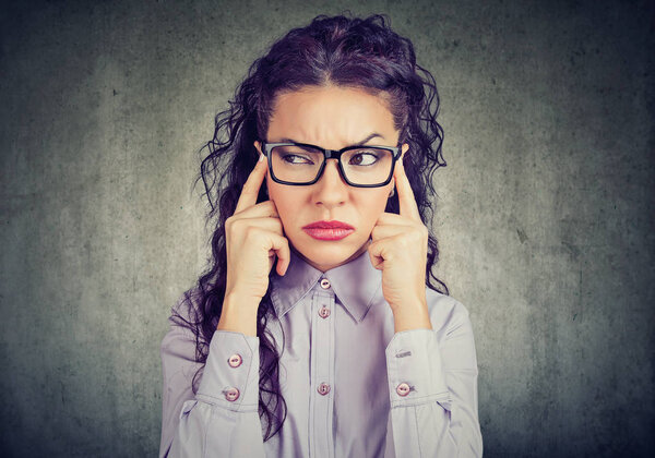 Curly brunette in glasses holding fingers on temples and concentrating on difficult decision looking away on gray background 
