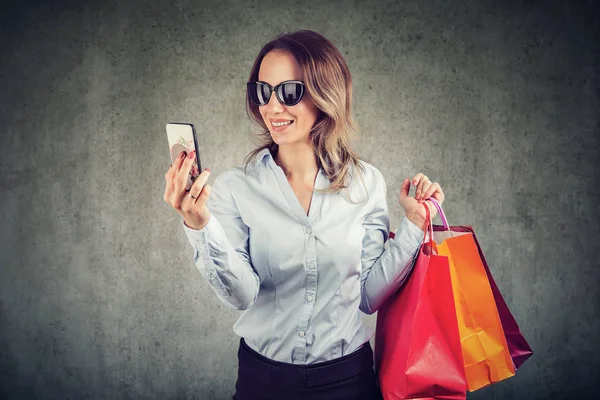 Güzel Genç Kadın Güneş Gözlüğü Smartphone Kullanarak Alışveriş Gidiyor — Stok fotoğraf