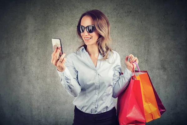 Güzel genç kadın güneş gözlüğü smartphone kullanarak alışveriş gidiyor 