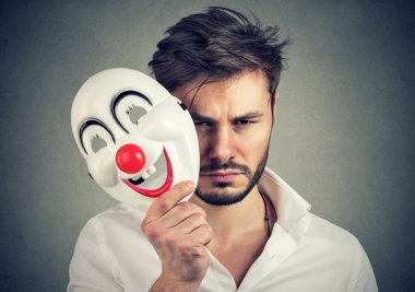 Mutlu maskesi tutarak ve gri arka plan üzerinde kameraya bakarken duygu üzgün ve kasvetli adam Genç sakallı