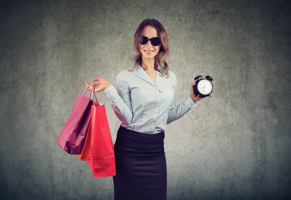 ショッピング バッグや灰色の背景に販売および割引のための時間を示すアラーム時計を保持しているスタイリッシュな女性 — ストック写真
