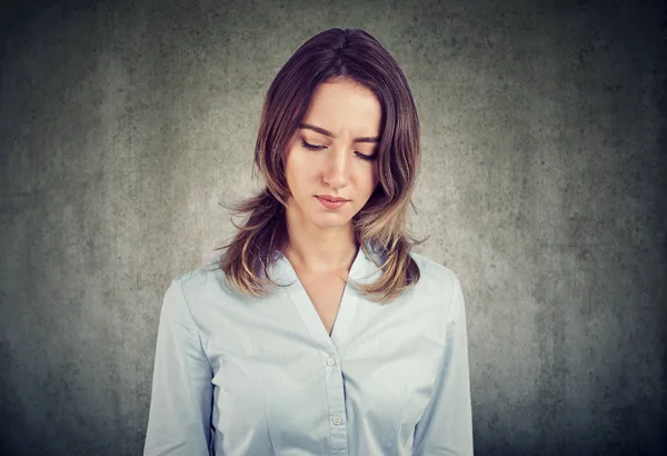 Genç güzel kadın gömlek gri arka plan üzerinde üzgün seyir kasvetli ve depresif duygular içinde aşağı bakıyor