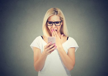 Gri arka plan üzerinde mesaj ile smartphone sörf ve seyir gözlüklü genç ifade sarışın kadın şok 