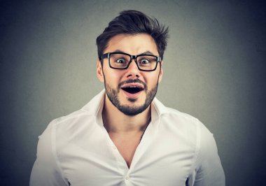 Adult man in white shirt and glasses looking stunned at camera with mouth opened on gray background clipart