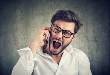 Telefon görüşmesi sahip ve gri arka plan üzerinde delilik ile bağırmaya gözlük ve Beyaz tişörtlü kaba öfkeli adam