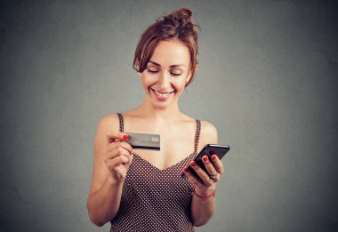 Online satın alma ve gri arka plan üzerinde gülümseyen yaparken Smartphone ve kredi kartı kullanan genç ve güzel kadın