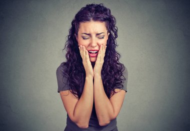 Diş ağrı ile acı ve gri arka plan üzerinde çığlık yanaklarda tutan genç kıvırcık esmer kadın eller