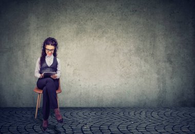 Zarif kadın sandalyede oturan ve gri arka plan üzerinde profesyonel çalışan olmanın tablet kullanma