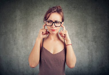 Uzak huysuz görünümlü ve gürültü kulaklarından kapsayan ve gri arka plan üzerine çatışma kaçınarak genç ve güzel kadın 