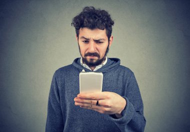Çatık genç adam sörf smartphone içinde antipati gri arka plan üzerine bıkkın
