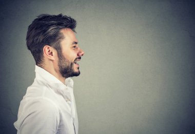 Genç yakışıklı yan görünüm uzağa bakarak ve gri arka plan üzerinde gülümseyen Beyaz tişörtlü adam sakallı