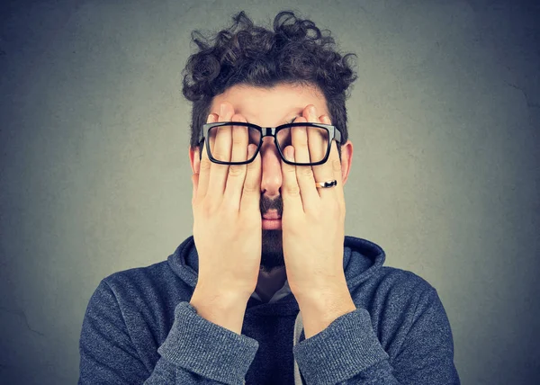 Portre portre genç adam gri duvar arka plan üzerinde izole iki elinizle yüzünü gözler kapsayan gözlük