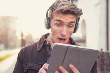 Modern genç adam hayretle ayakta tablet Caddesi üzerinde sörf kulaklık