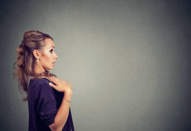 Modern genç kadın göğüs içinde sürpriz uzakta gri arka plan üzerinde seyir üzerinde elini tutarak yan görünüm