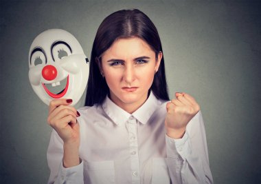 Young woman with split personality looking super angry at camera while holding clown mask to hide clipart