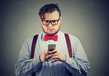 Cep telefonu gri duvar arka plan üzerinde izole alınan metin mesajı yanıtlamak düşündüğüm karışık ciddi görünümlü bir adam. Yüz ifadesi 