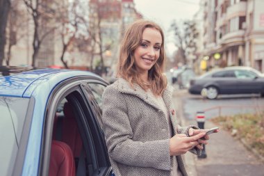 Arabasının yanında duran cep telefonu kullanan mutlu kadın