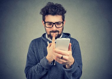 şaşkın adam ne cep telefonu gri duvar arka plan üzerinde izole alınan metin mesajı yanıtlamak düşünüyor. Yüz ifadesi tepki beden dili