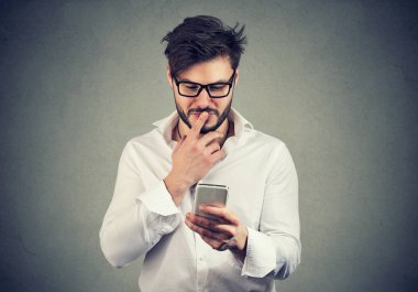 şaşkın adam ne cep telefonu gri duvar arka plan üzerinde izole alınan metin mesajı yanıtlamak düşünüyor. Yüz ifadesi tepki beden dili