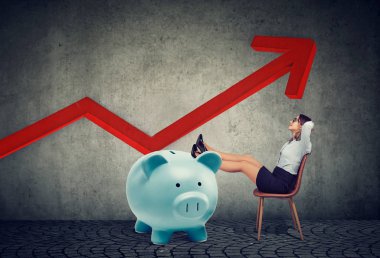 büyük piggy banka ve finansal grafik sandalyede oturan rahatlatıcı kadar büyüyen genç iş kadını