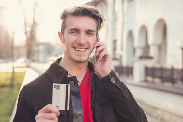 Счастливый Молодой Человек Говорит Смартфоне Показывая Кредитную Карту Глядя Камеру — стоковое фото