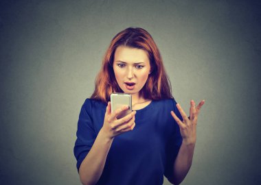 Genç Kızıl saçlı kadın okuma mesaj Smartphone cep telefonu ile gri arka plan üzerinde şaşkın bakıyor