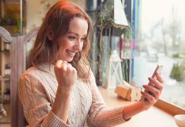 Akıllı telefonu kafede otururken izlemek euphoric süper heyecanlı kadın 