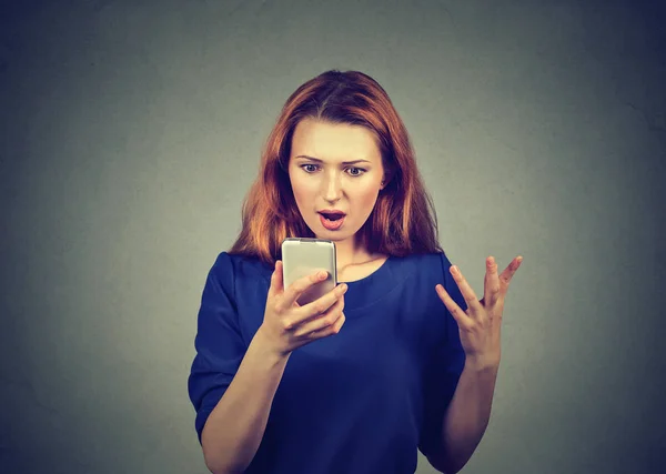 Молодая Рыжая Женщина Читающая Сообщение Смартфоне Выглядит Ошеломленной Сером Фоне — стоковое фото