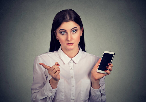 Formal irritated woman in white shirt holding smartphone and shaking with finger giving bad review on gray background