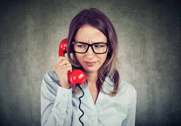 灰色の背景の赤い電話に話している間混乱と疑問を探している若い女性 — ストック写真