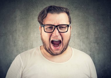 Gözlük kamera gri arka plan üzerinde öfke içinde bağırıyor genç casual tombul adam