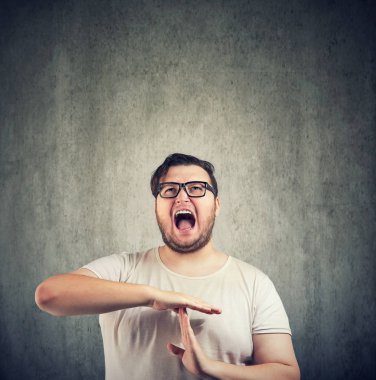 Casual obez adam sıkıntı içinde bağırıyor ve gri arka plan üzerinde zaman aşımı için el hareketi gözlük