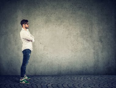 Casual modern adam beyaz gömlek ve denim ayakta gri duvar arka plan karşı yan görünüm