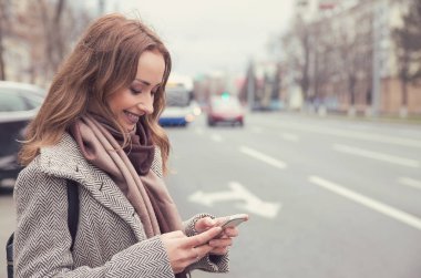 Gülümseyen casual kadın bir otobüs beklerken cep telefonu üzerinden e-posta kontrol 