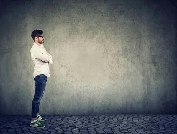 Casual modern adam beyaz gömlek ve denim ayakta gri duvar arka plan karşı yan görünüm