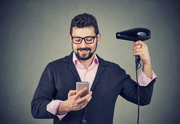 Happy man reading news on smartphone blowing hair with hairdryer — Stock Photo, Image