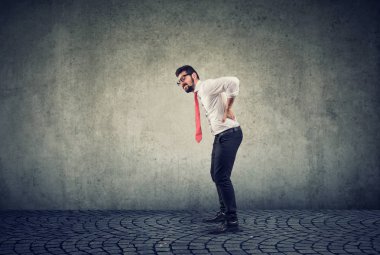 Gri arka planda sırt ağrısı olan genç iş adamı 