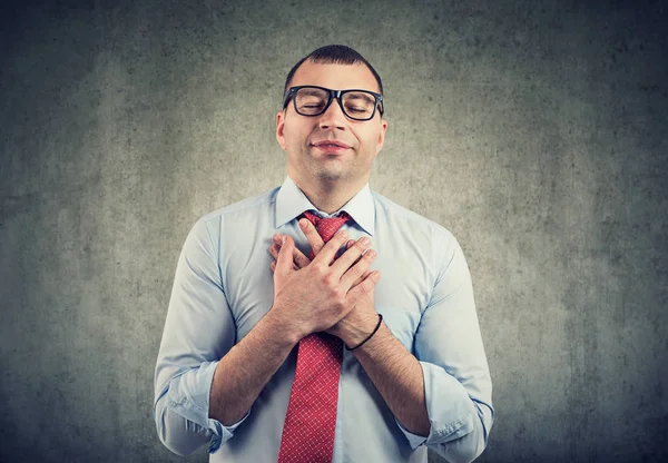 Geschäftsmann mit geschlossenen Augen hält die Hände auf der Brust in Herznähe, zeigt Freundlichkeit — Stockfoto