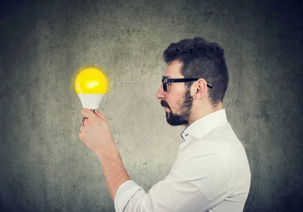 Hombre de negocios con expresión reflexiva mirando bombilla brillante — Foto de Stock