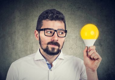Meraklı adam parlak ampul bakarak tutarak 