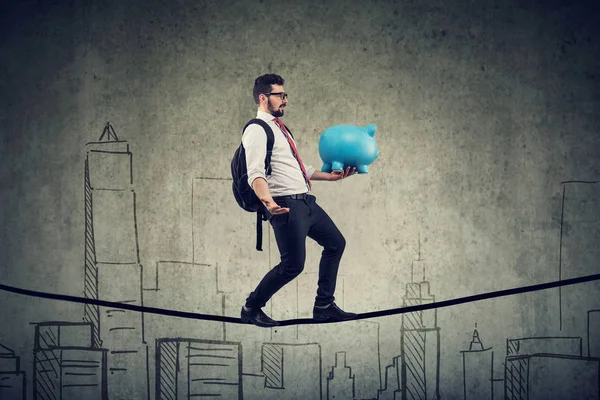 Man met rugzak en Piggy Bank lopen balanceren op een touw boven een skyline van de stad — Stockfoto