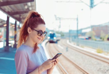Metro platformunda cep telefonunu kullanan genç kadın, mesaj sms e-posta veya tren programı kontrol. 