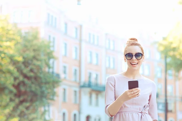 Молодая стильная симпатичная женщина с помощью смартфона ходит по улице — стоковое фото