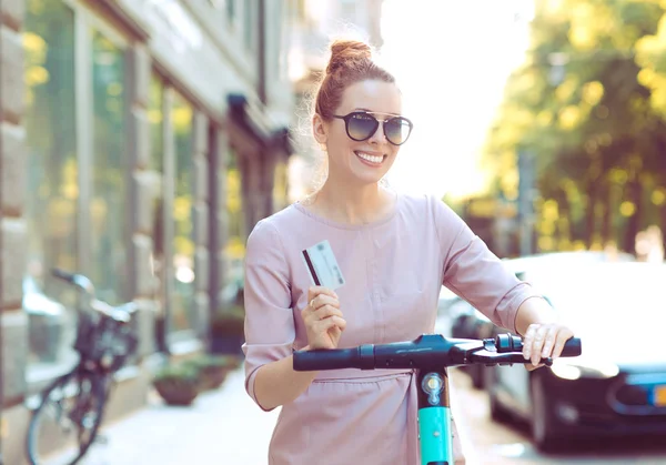 Mujer cool con tarjeta de crédito alquilando un scooter eléctrico listo para explorar la ciudad —  Fotos de Stock