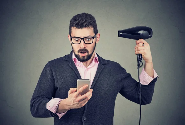 Шокований чоловік перевіряє телефон, який тримає фен — стокове фото