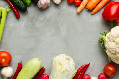 Gri arka planda çeşitli çiğ sebzeler. Ortasında fotokopi alanı var. Kabak, salatalık, biber, mantar, domates, karnabahar, marul, havuç, kereviz, sarımsak, kırmızı biber.